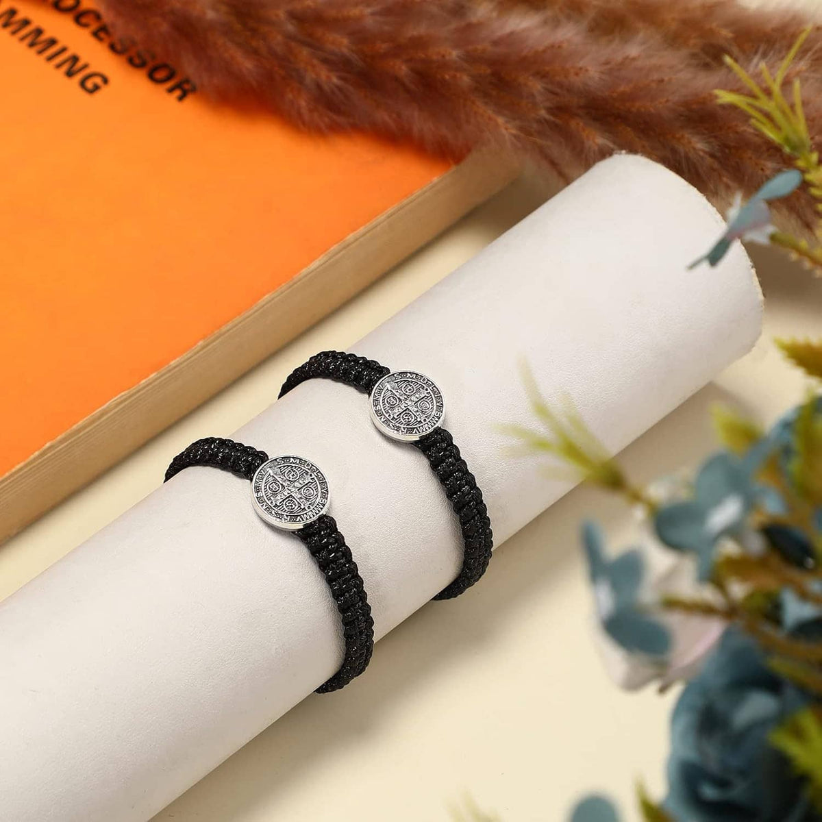 Two black braided bracelets with silver medal charms on a white card