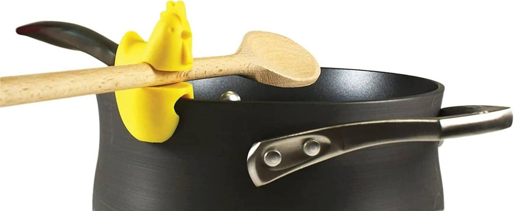 Yellow chicken-shaped silicone spoon rest clipped to black pot with wooden spoon