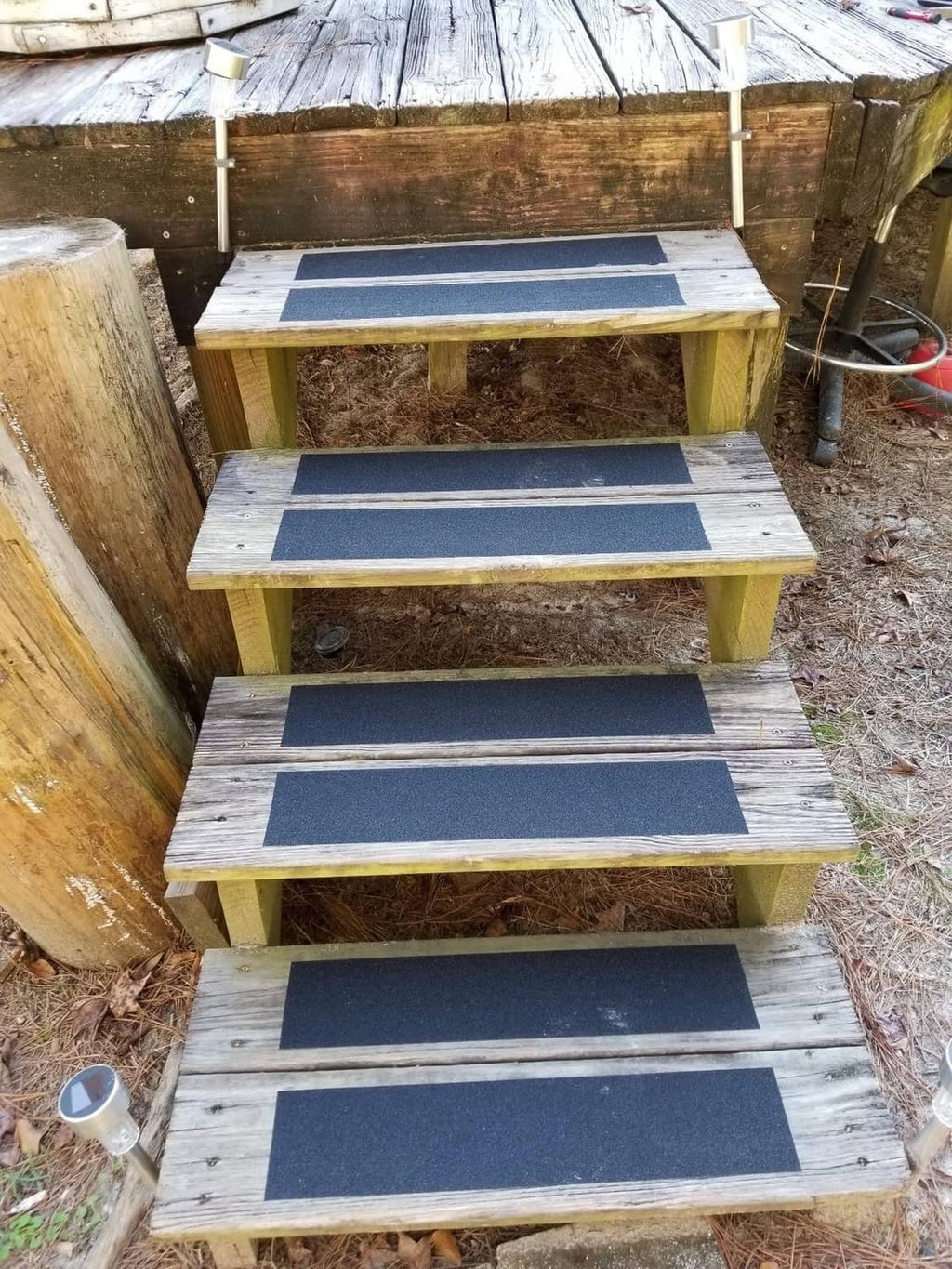 Anti-slip tape strips applied to wooden outdoor steps, dark gray rectangles