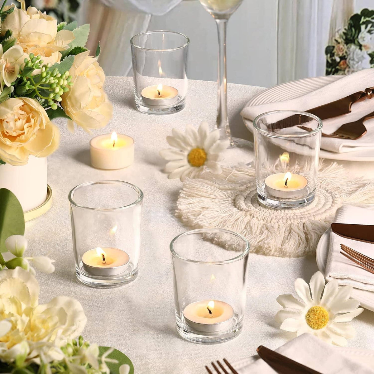Multiple clear glass tea light holders with lit candles on a decorated table