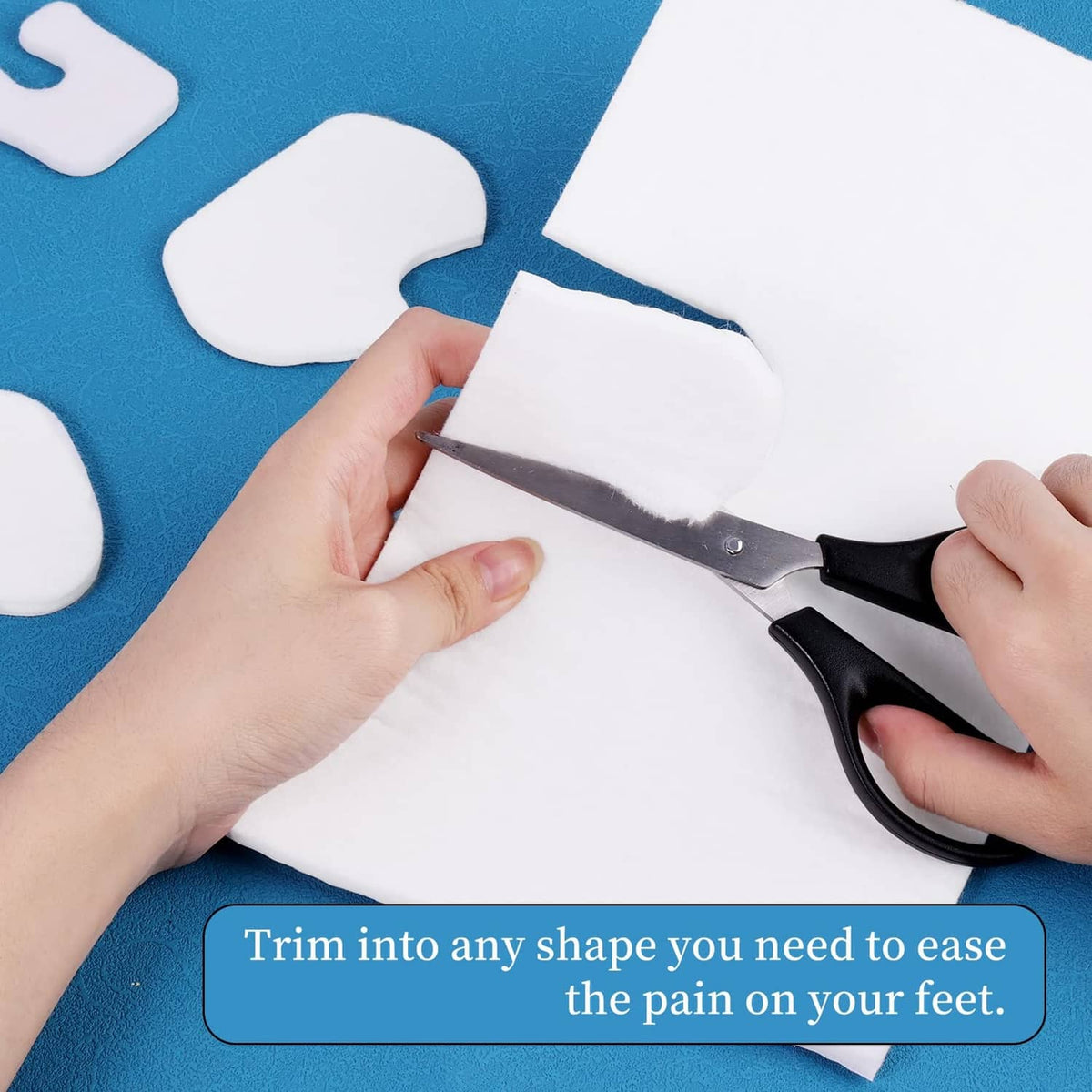 Hands trimming white adhesive felt into custom foot pad shapes with scissors.