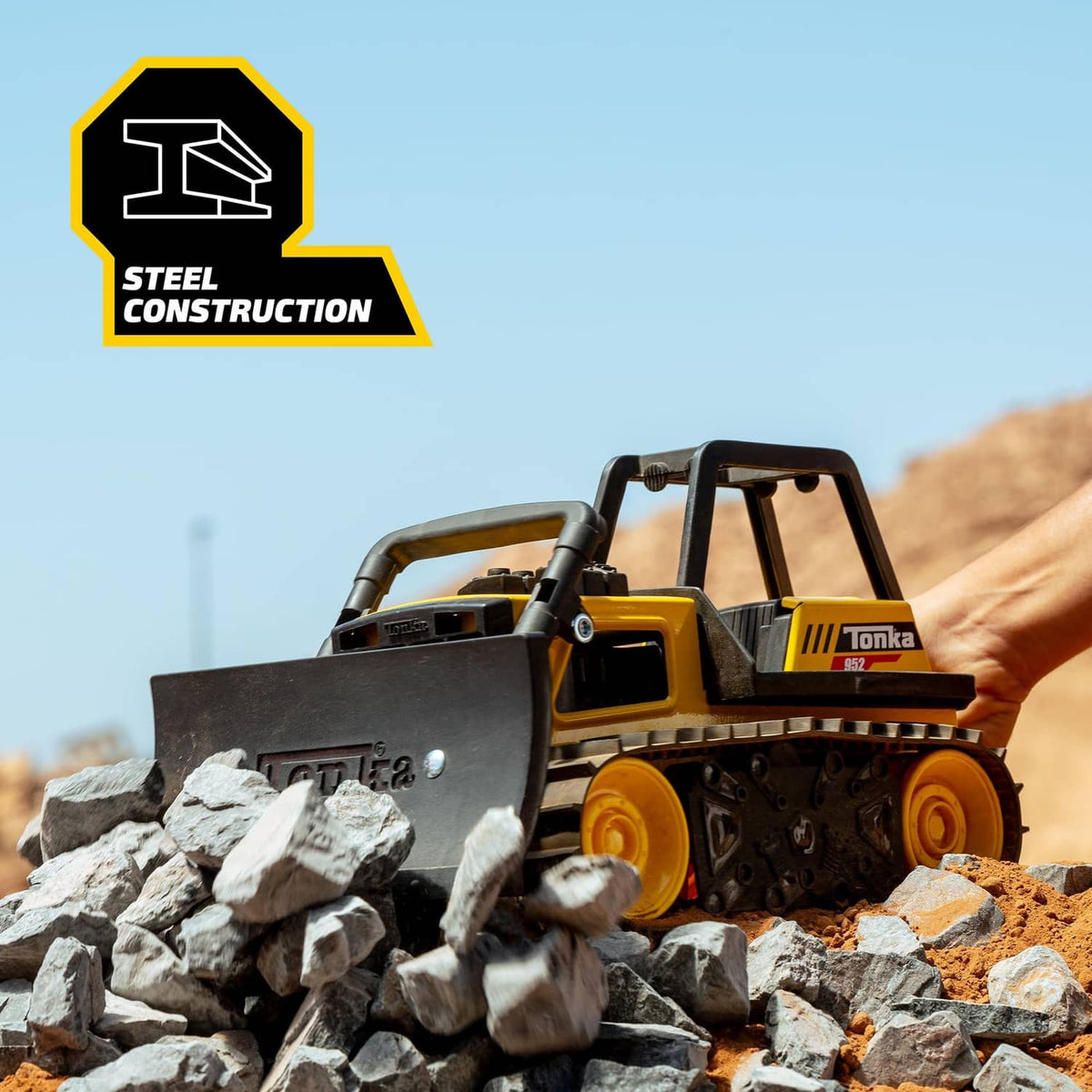 Yellow Tonka bulldozer toy on rocks with lowered front blade