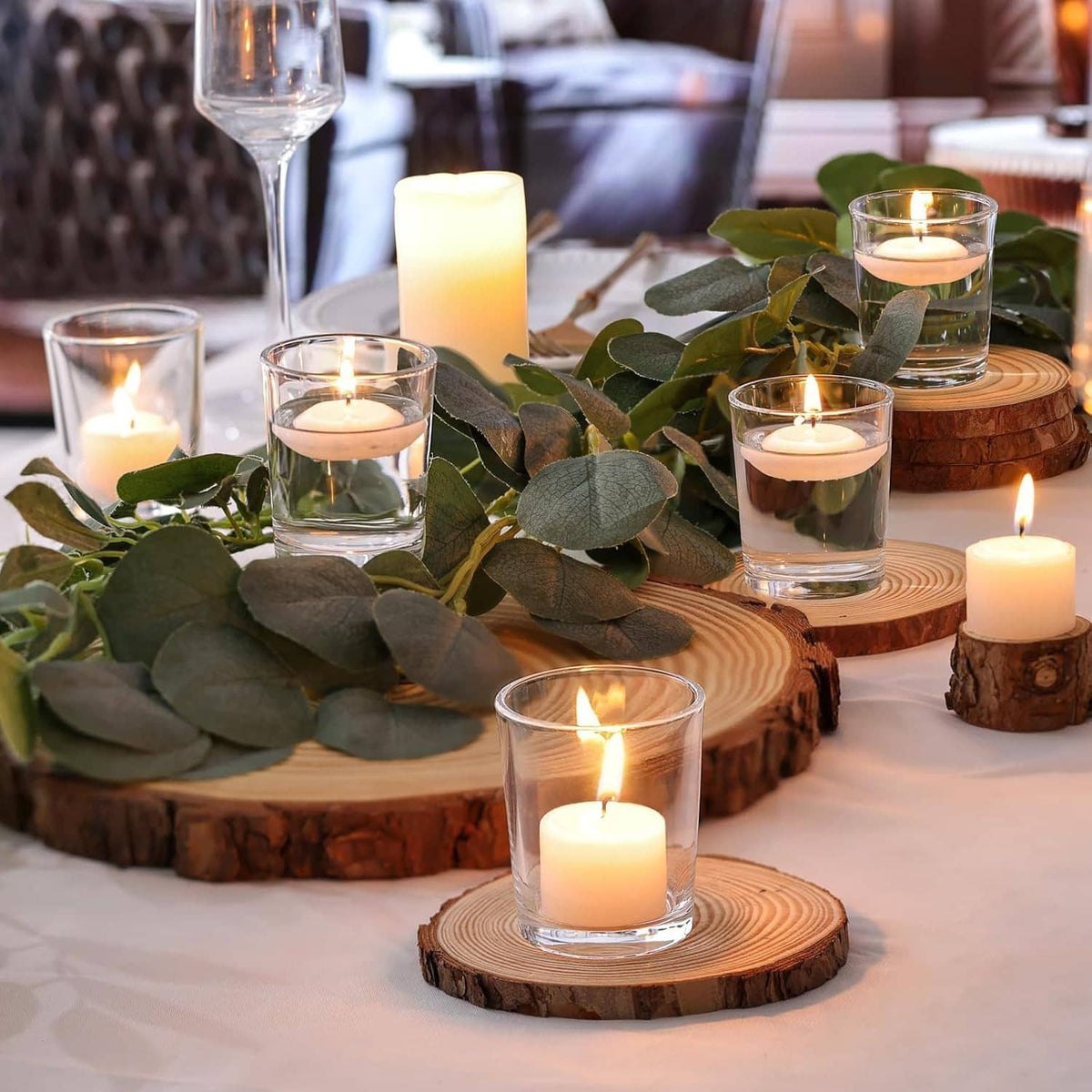 Clear glass candle holders with lit tea lights on round wood slices at an event table