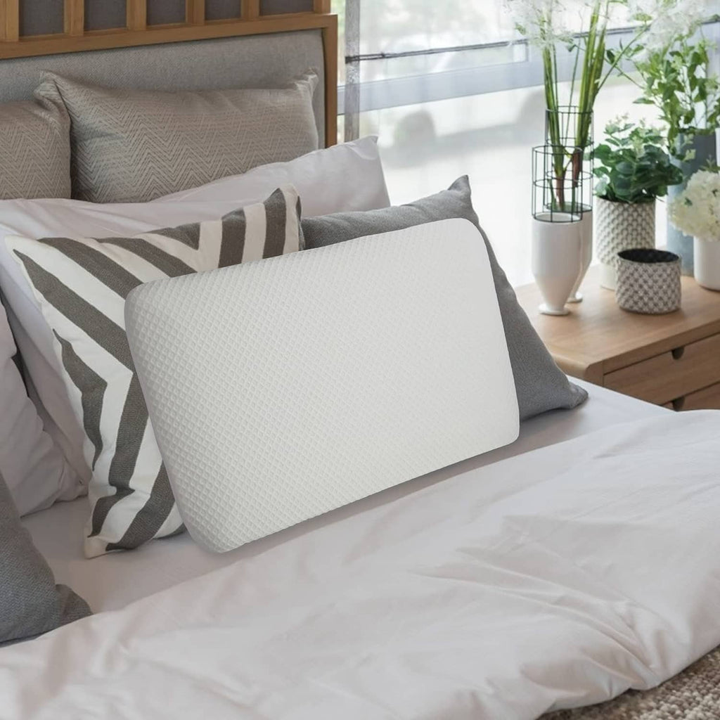 White flat memory foam pillow on bed surface next to a striped cushion.