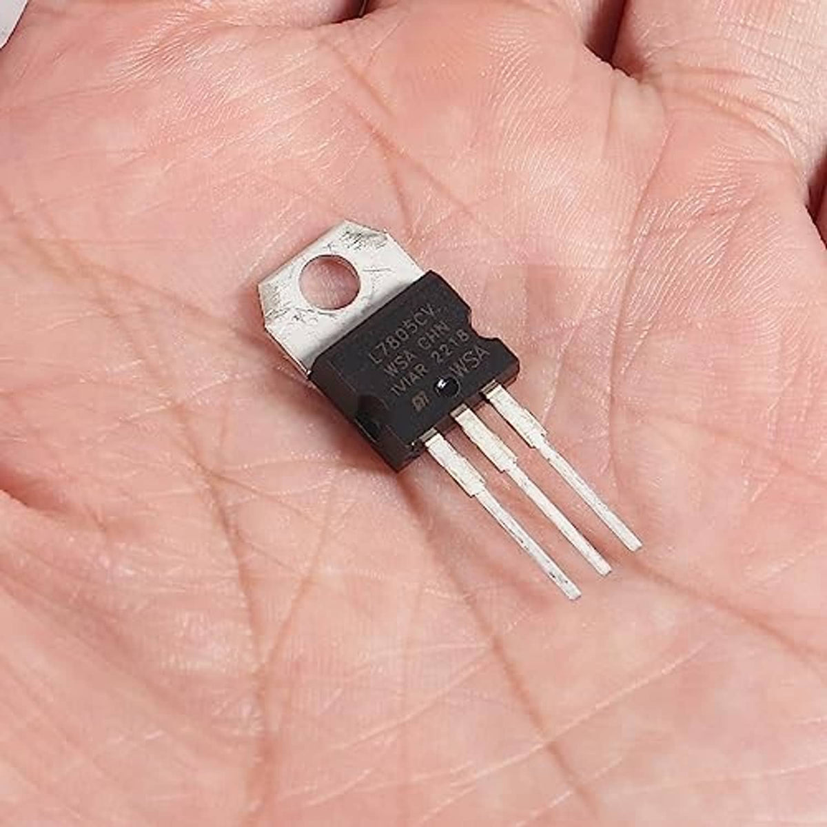 L7805CV 5V regulator IC on palm, metal tab mounting hole, three pin leads