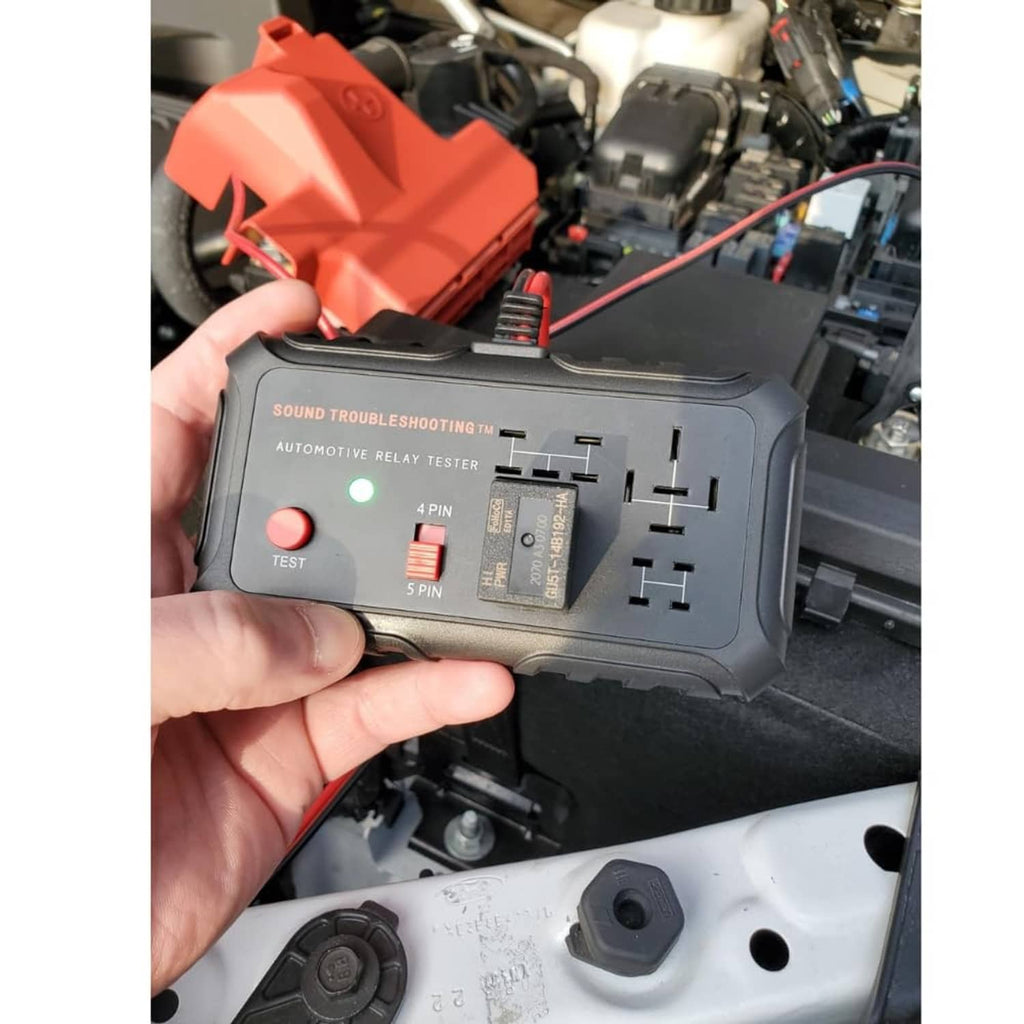 Close view of automotive relay tester in hand over car relay area with red module