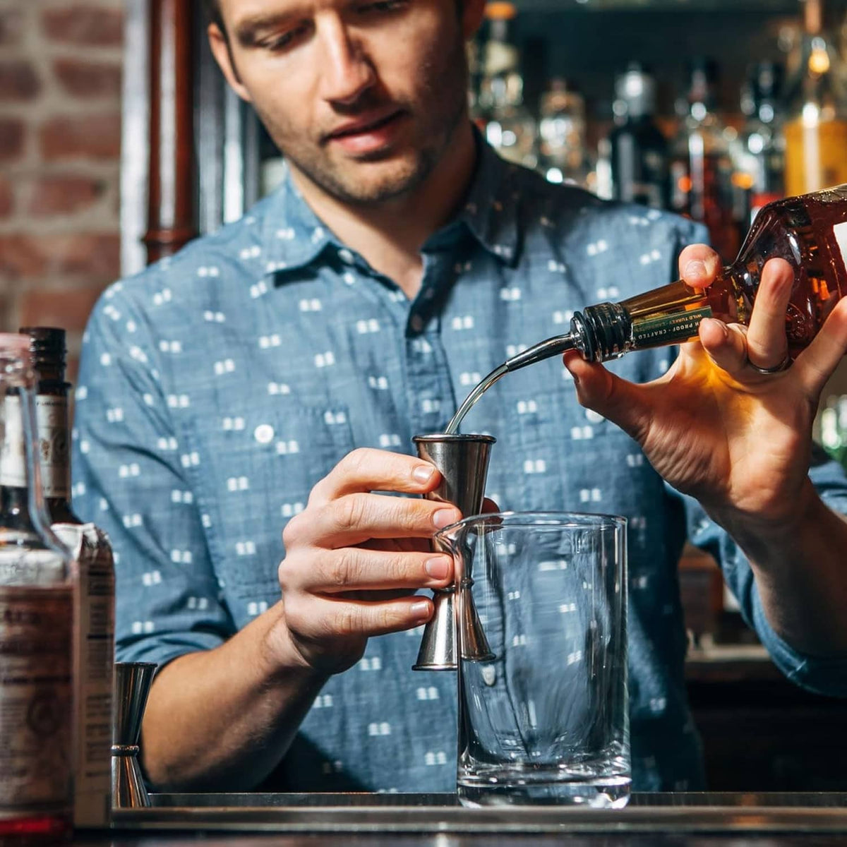 Stainless steel jigger in use at a bar, held over a mixing container