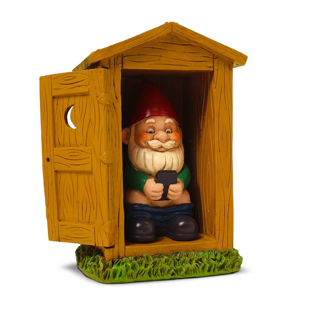 Toilet garden gnome statue in wooden outhouse, red hat, holding a dark tool