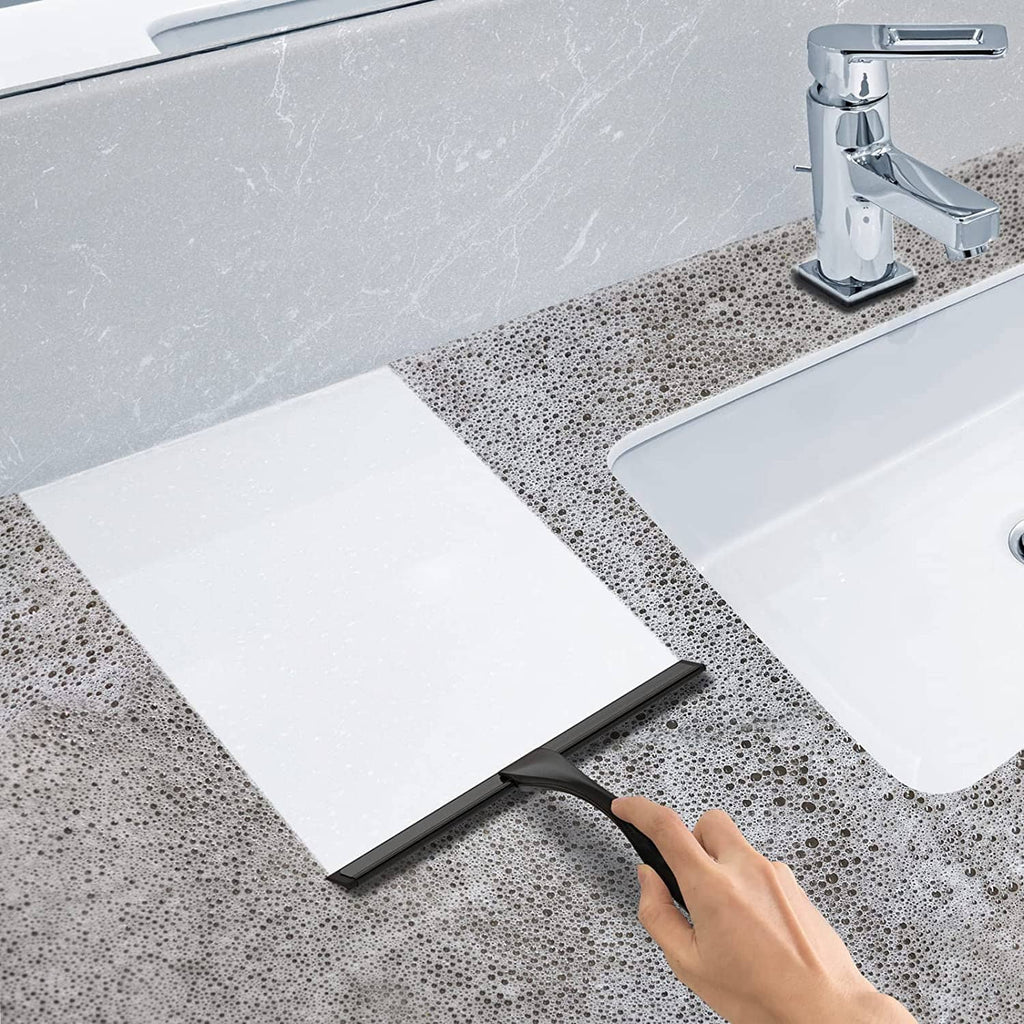 Black squeegee clearing water from a wet countertop edge near a faucet.
