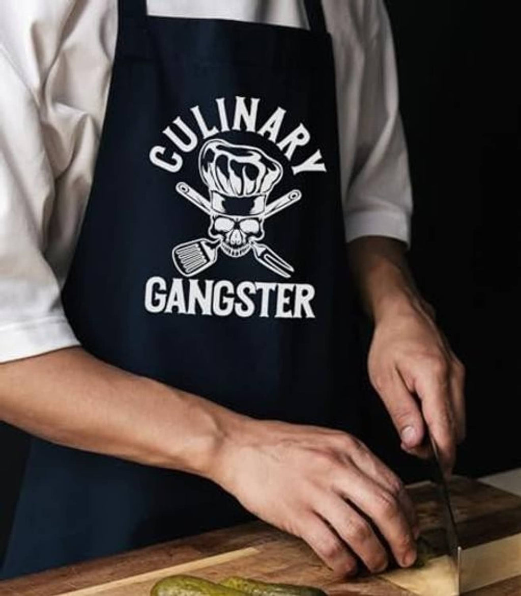 Black apron with skull and utensils graphic, worn while cutting on a wooden board.