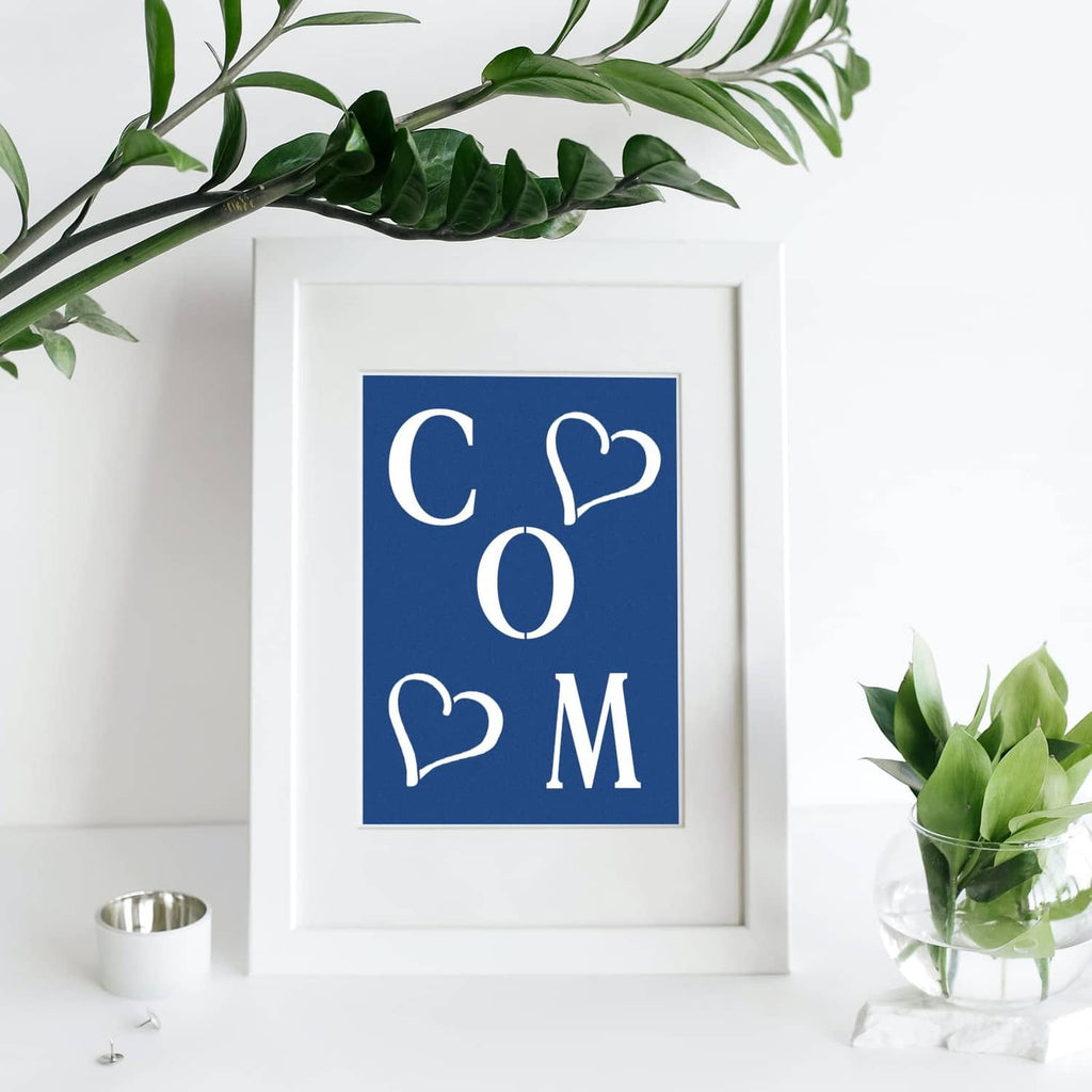 Framed stencil design with letters “C O M” and heart outlines on a blue panel