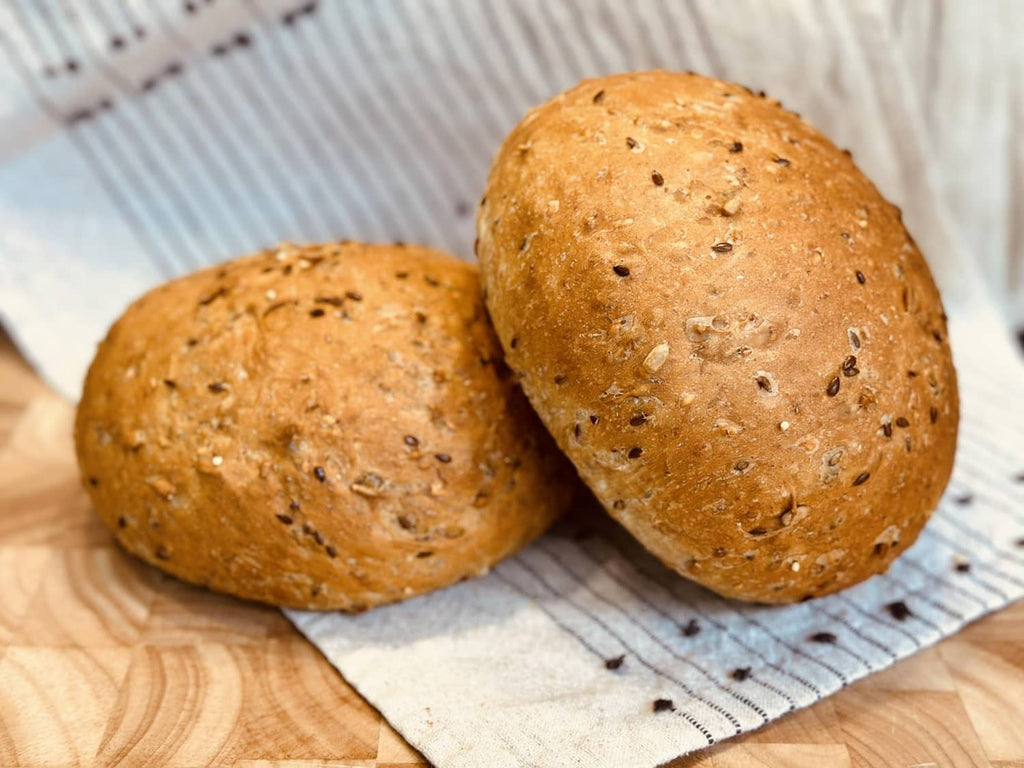 Two round 8 grain bread rolls with speckled seeded crust on a cloth