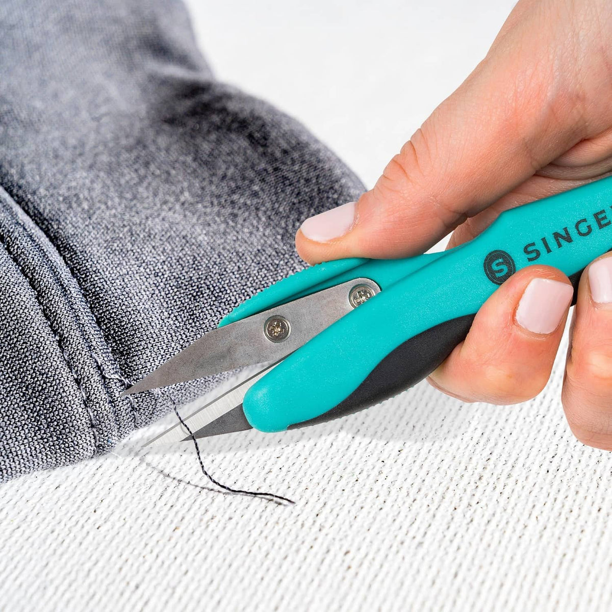 Close-up of teal thread snips snipping threads near a stitched seam