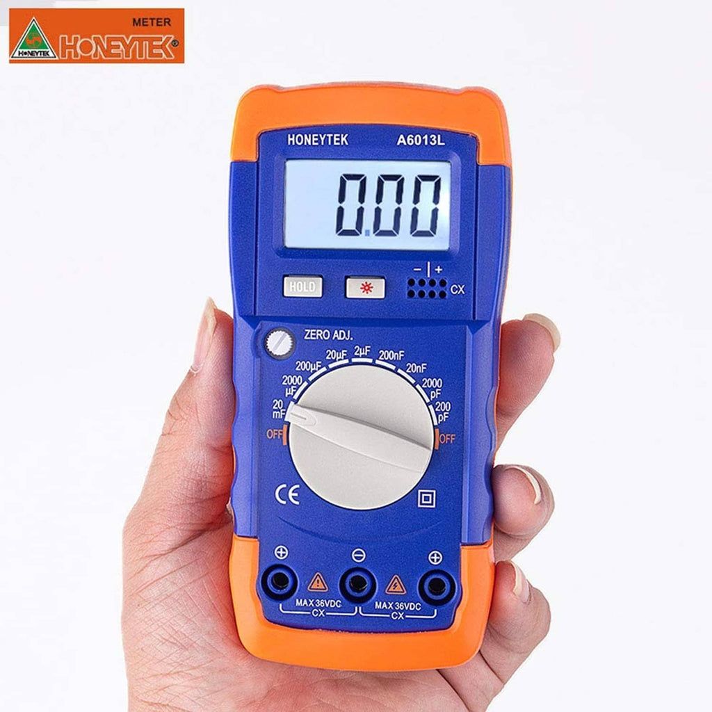 Handheld capacitor tester in hand, orange-blue body and LCD display showing 0.000