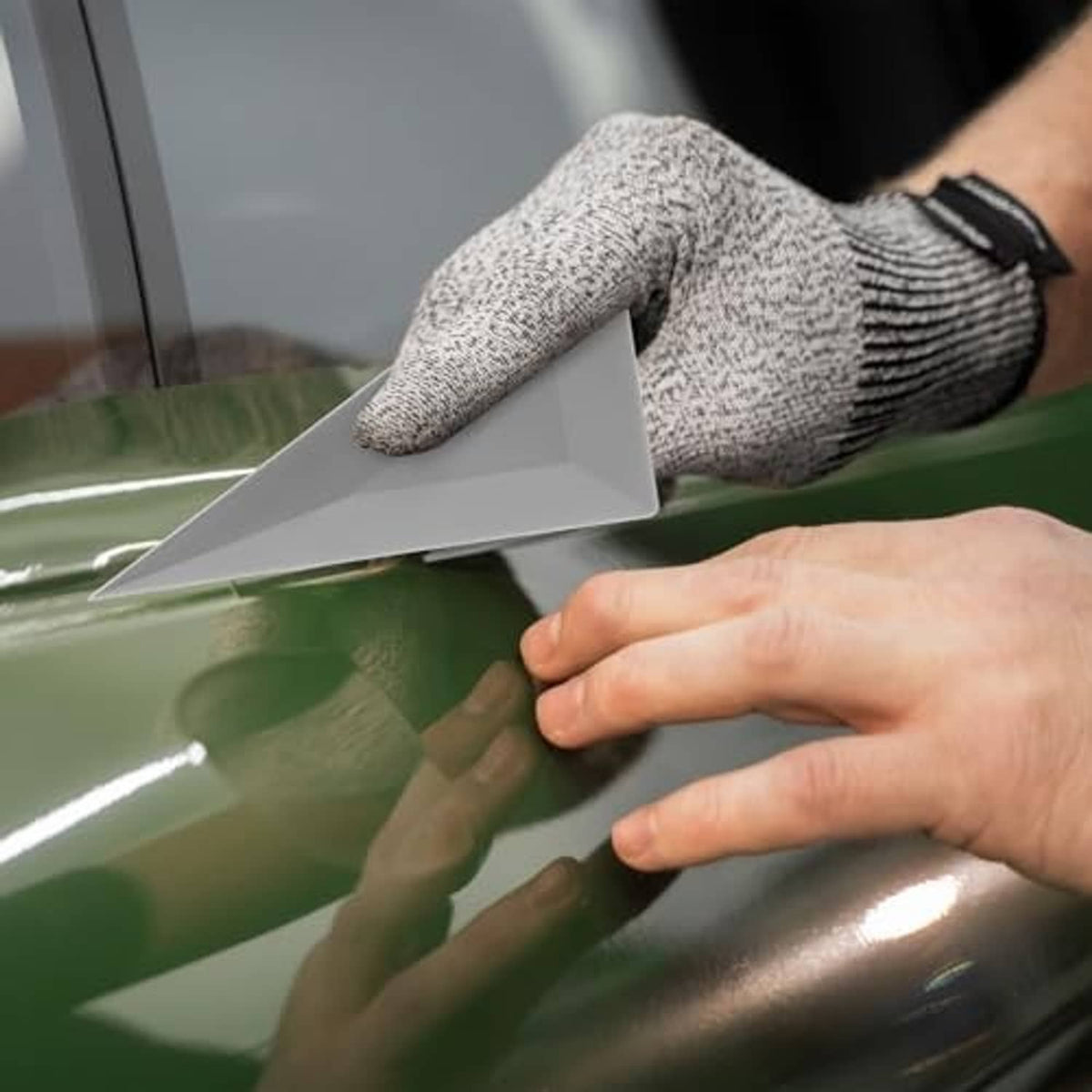 Hand using gray triangle tint squeegee card to smooth green window film