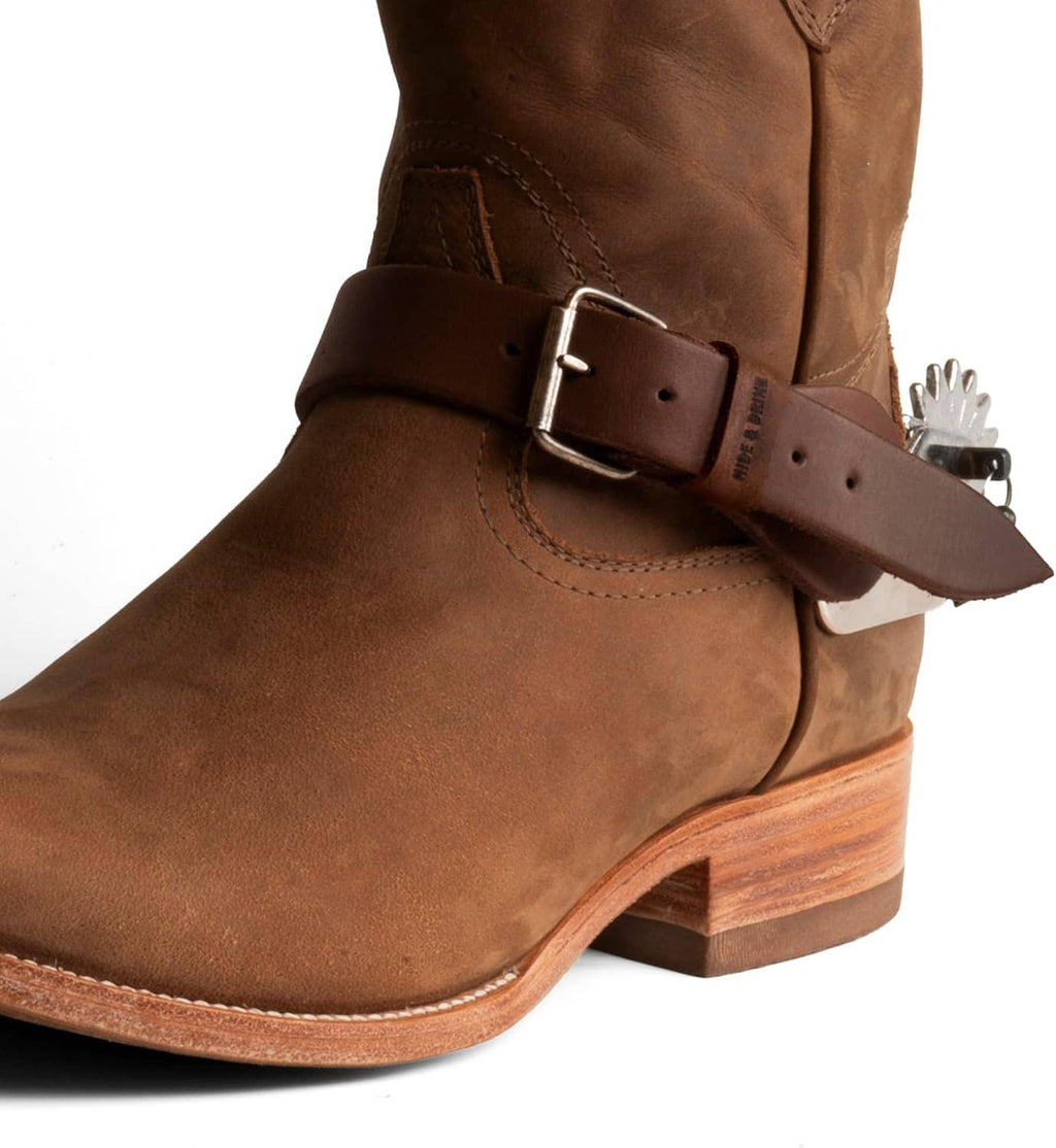 Brown leather spur strap with adjustable metal buckle on cowboy boot shaft