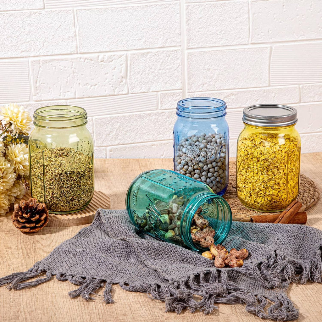 Assorted colored wide-mouth mason jars with metal lids, including teal and yellow, on a blanket.