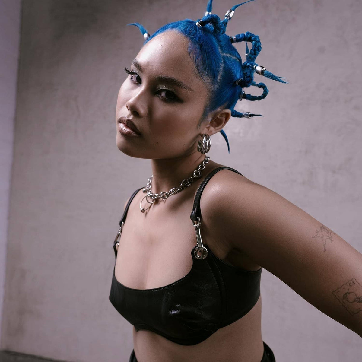 Woman with vivid blue hair in braided spikes, wearing a black strappy top