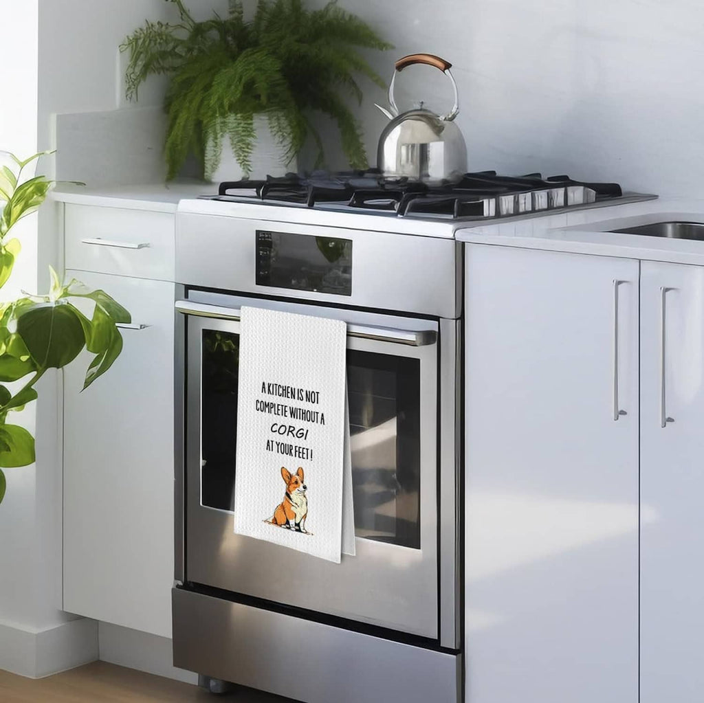 White waffle weave kitchen towel hanging on oven door, featuring corgi illustration and message.