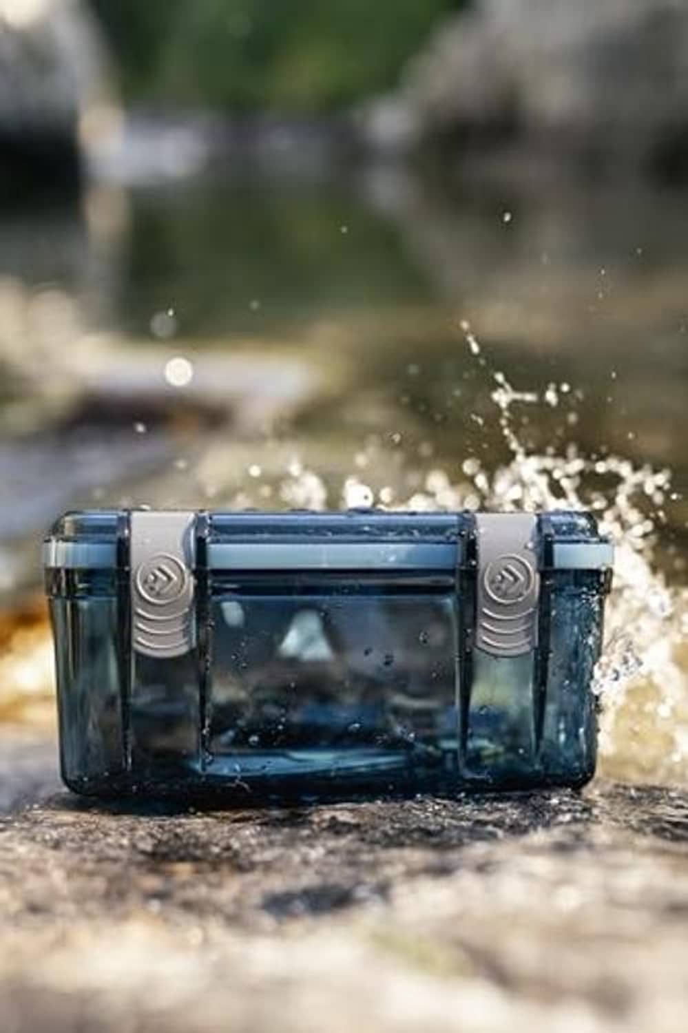 Blue watertight box with clear window and sealed hinged lid, water splashes on rock