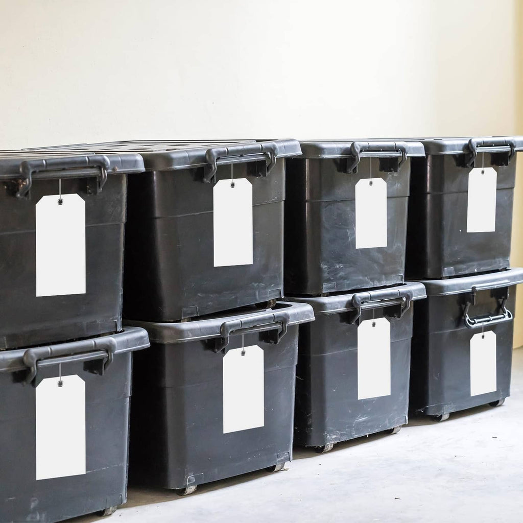 White plastic shipping tags with round hole, multiple tags clipped to black storage bins