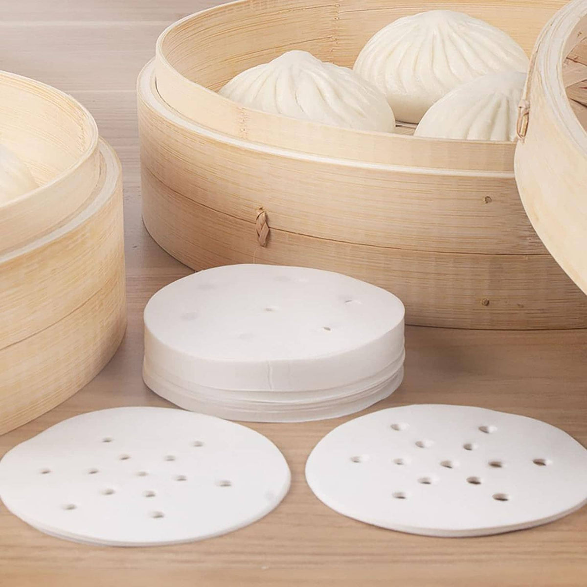 Stack of round white steamer liners with small holes, in a bamboo steamer basket
