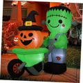 Green Frankenstein inflatable holding an orange pumpkin with black witch hat, standing outdoors