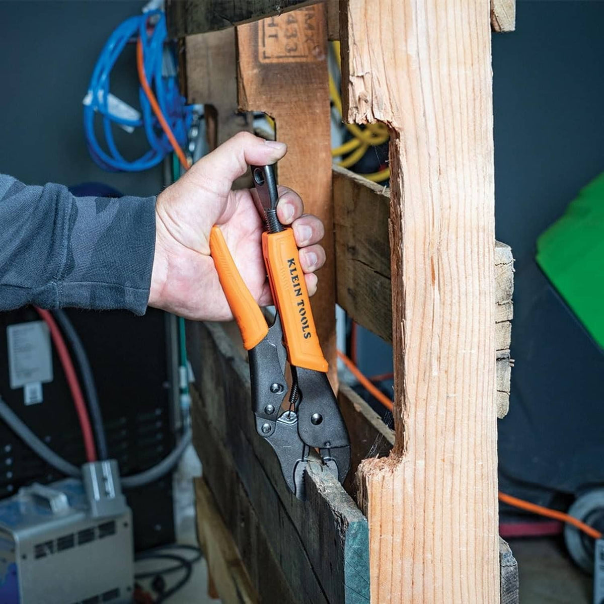 Orange-and-black locking pliers held by hand beside wood and wiring