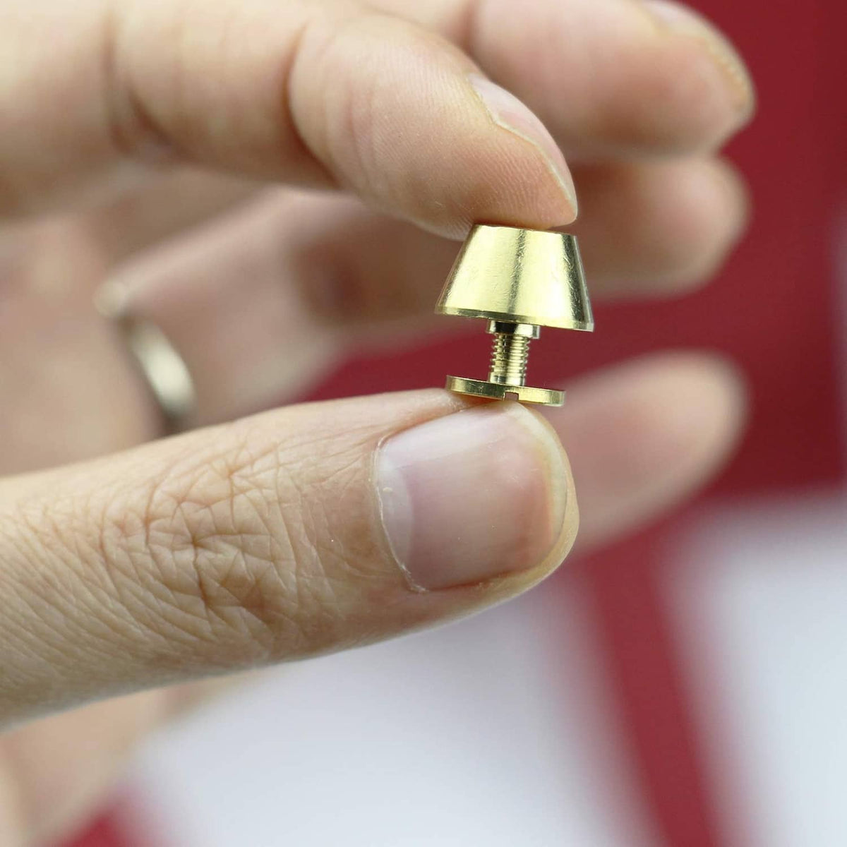 Close-up of a hand attaching a round brass screw-back handbag foot