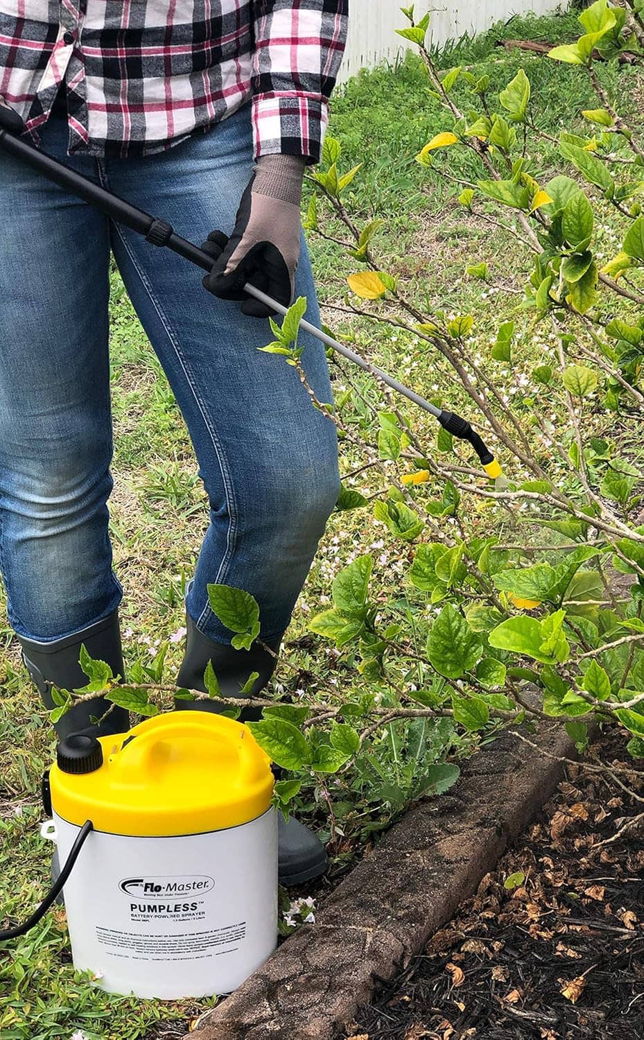Yellow tank battery sprayer with black wand spraying into a garden bed