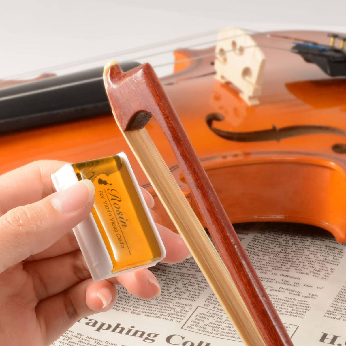 Rosin block held near a violin bow and instrument, for violin/viola/cello