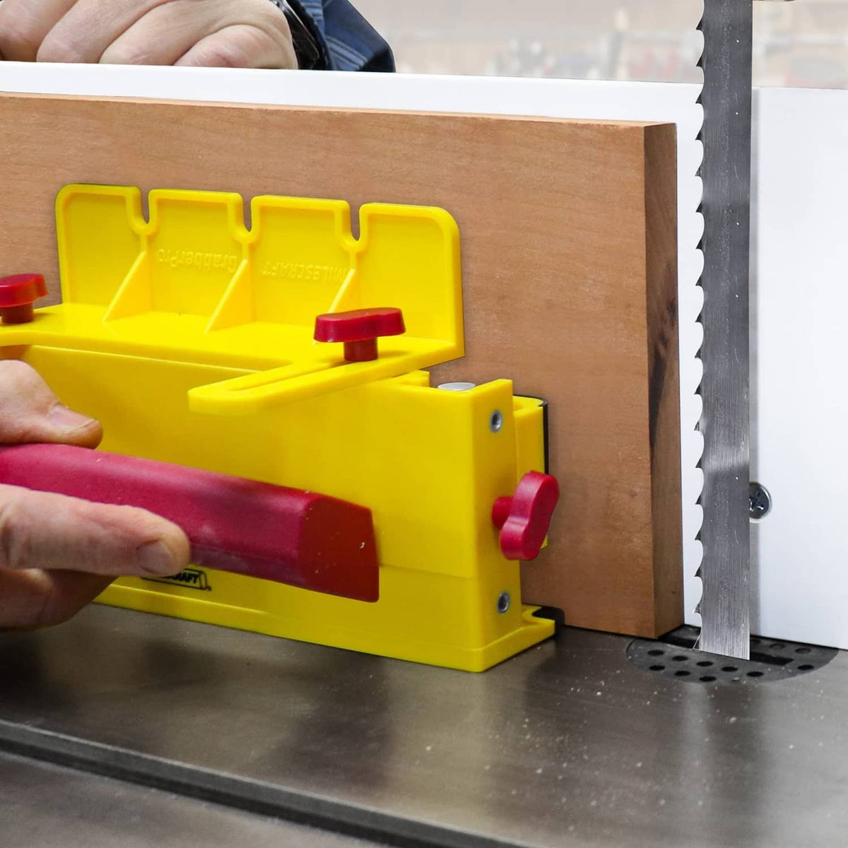 Yellow push block with maroon handle and side knob, gripping a board against the fence