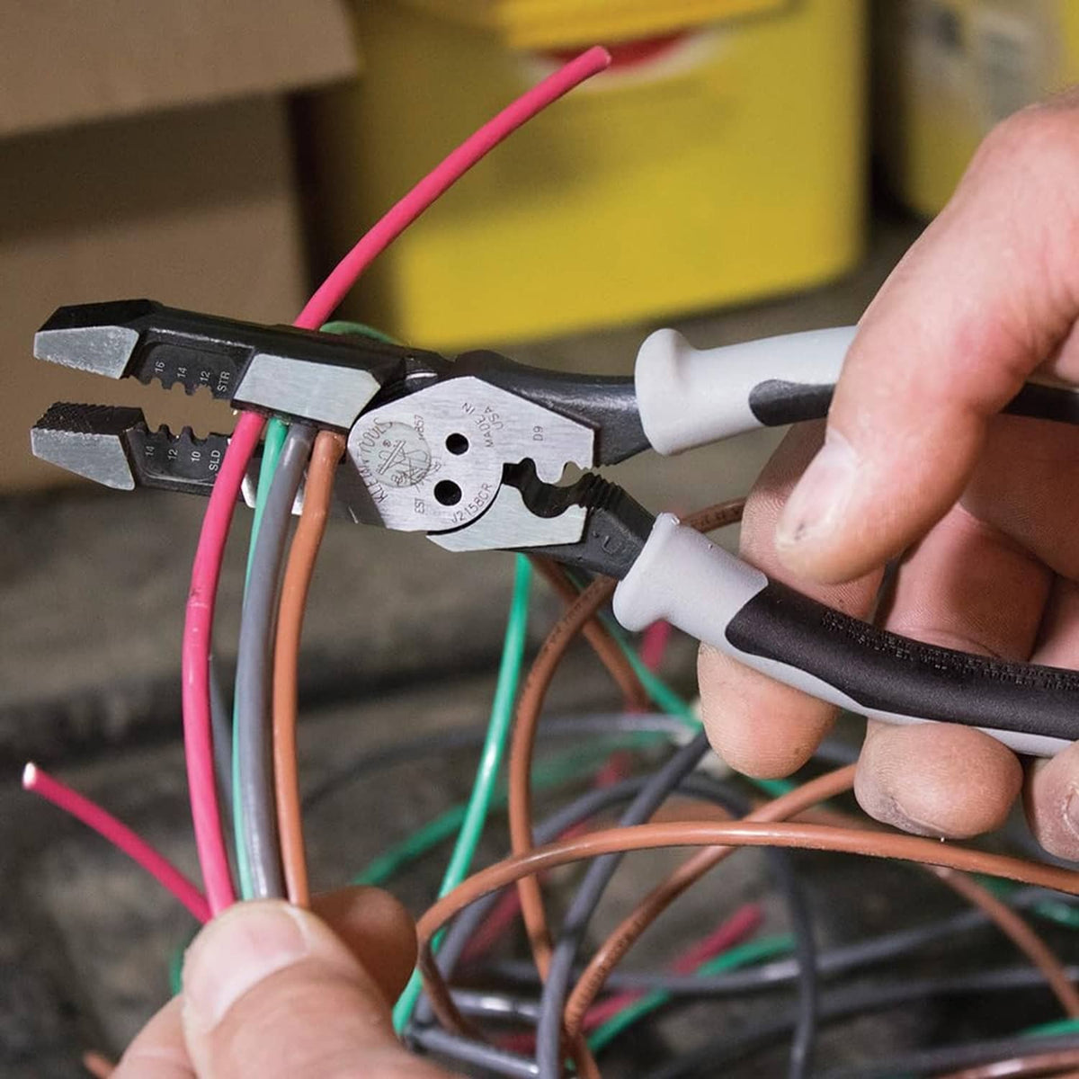 Hybrid multitool pliers gripping and crimping colored electrical wires in a panel