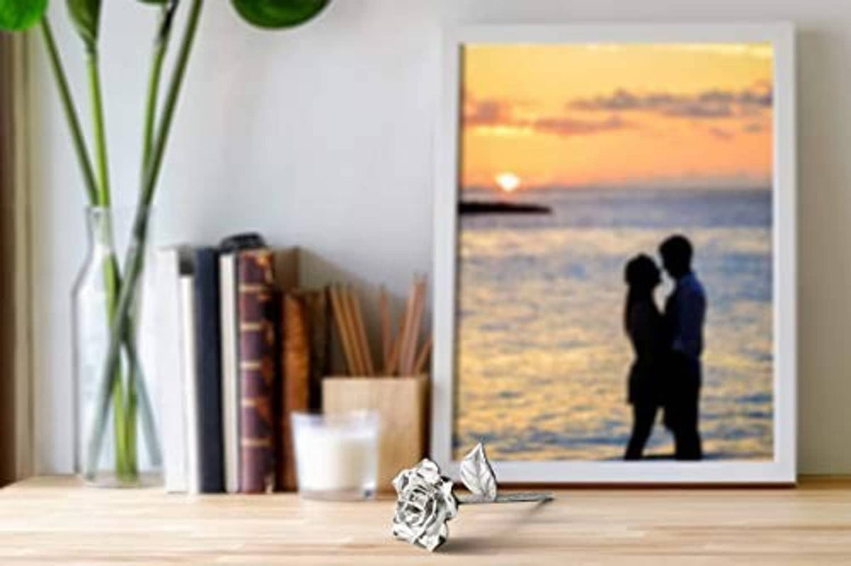Silver tin rose ornament on a tabletop near a framed ocean scene