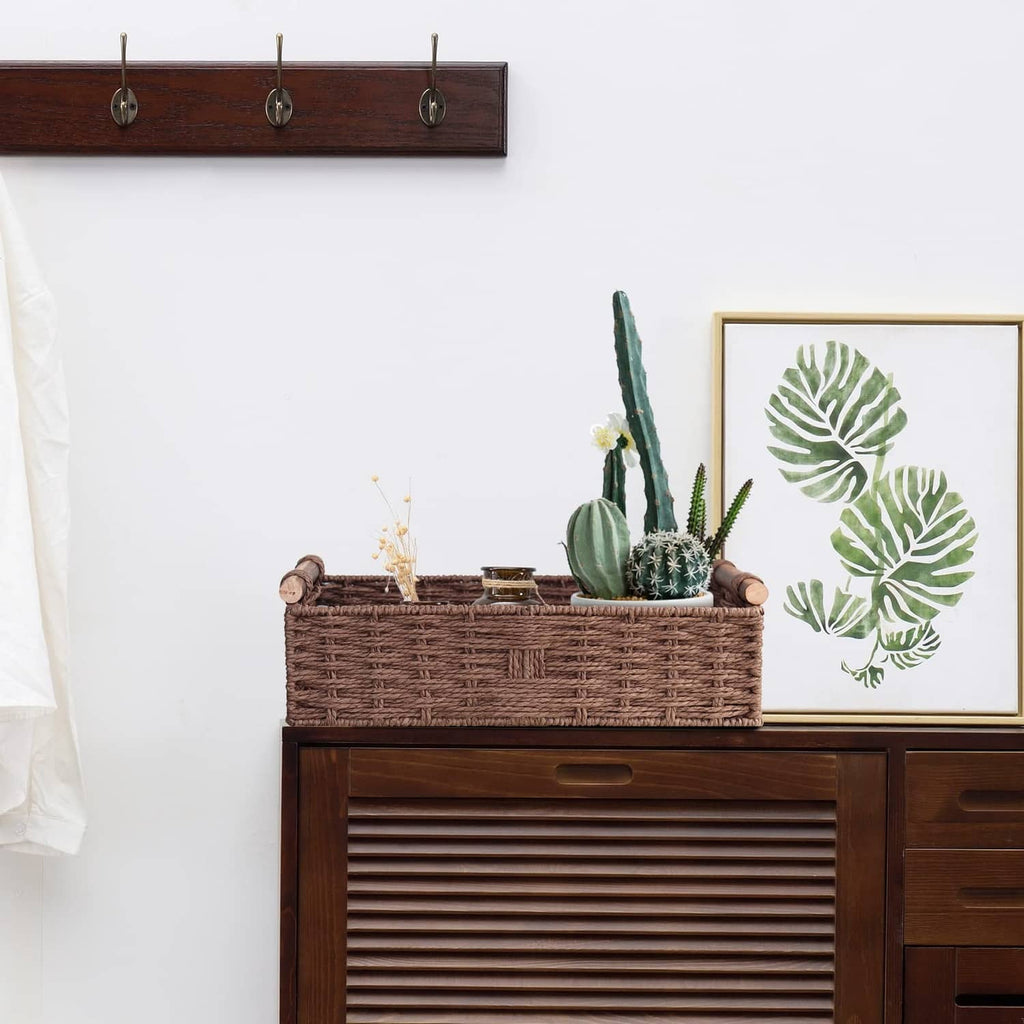 Brown woven basket with side handles on wood cabinet, holding small plants