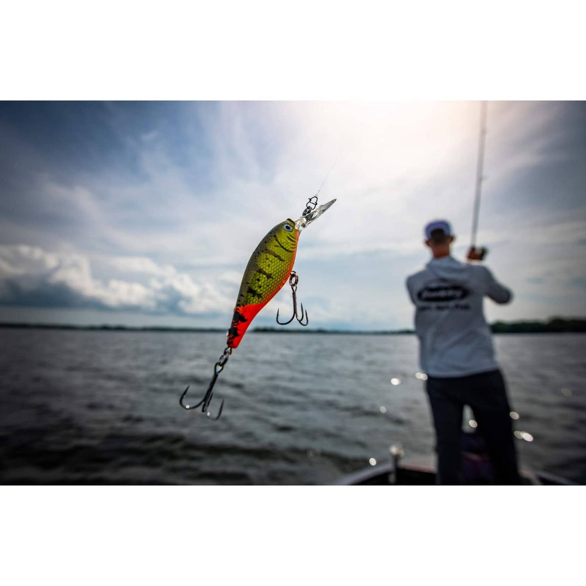 Green, red, and black crankbait fishing lure with treble hooks in midair over water.
