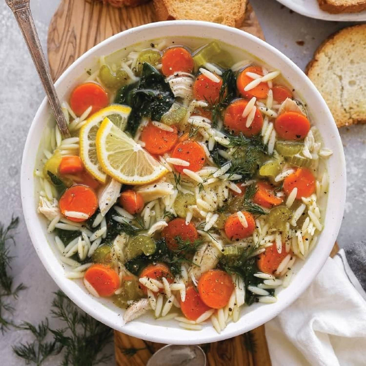 Bowl of soup with noodles, carrots, greens, and lemon garnish
