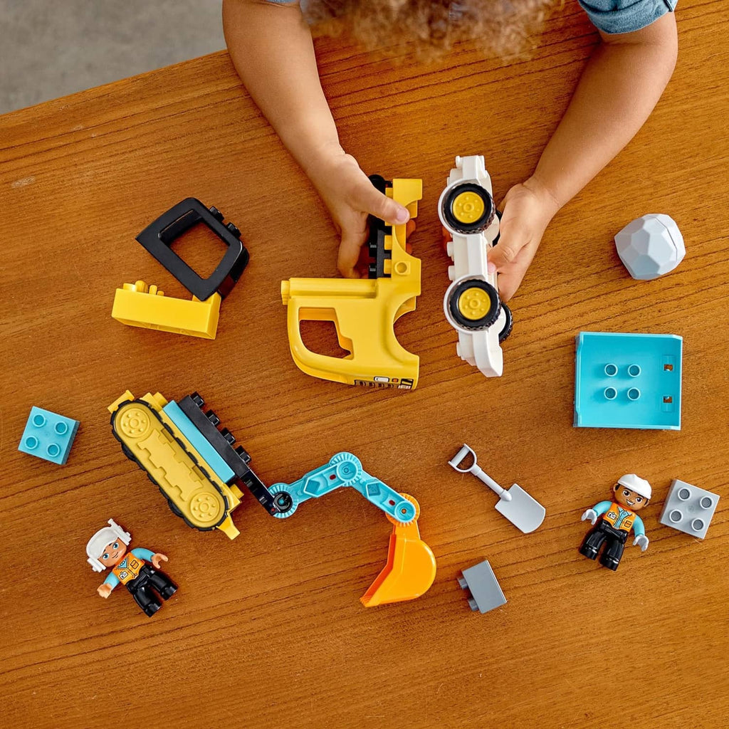 Hands assembling yellow and blue construction vehicles with DUPLO blocks and worker figures