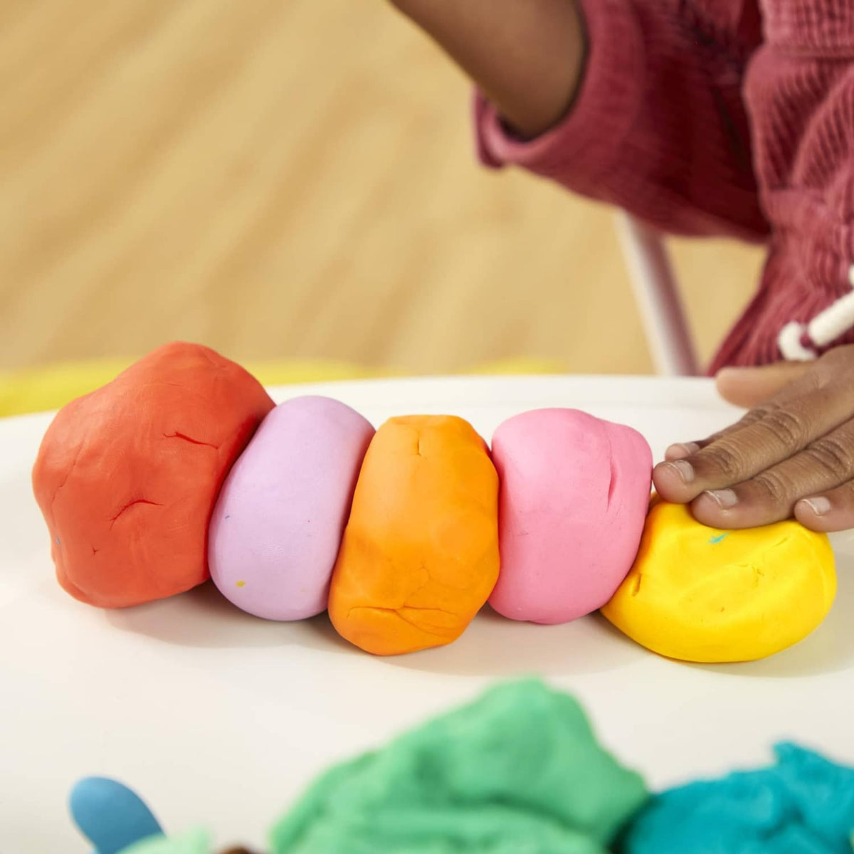 Hands molding multicolor Play-Doh clay on a tabletop