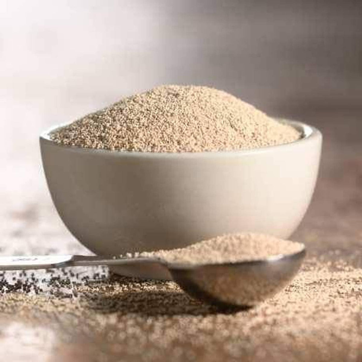 Instant yeast powder in white bowl and on spoon, beige granules for baking.
