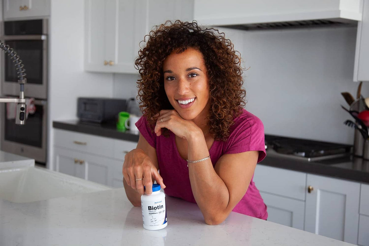 Woman holding a biotin supplement bottle with blue cap in a kitchen