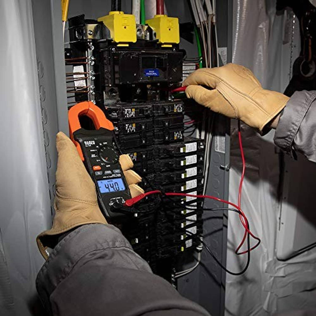Digital clamp meter in a breaker panel with blue display reading and test leads.