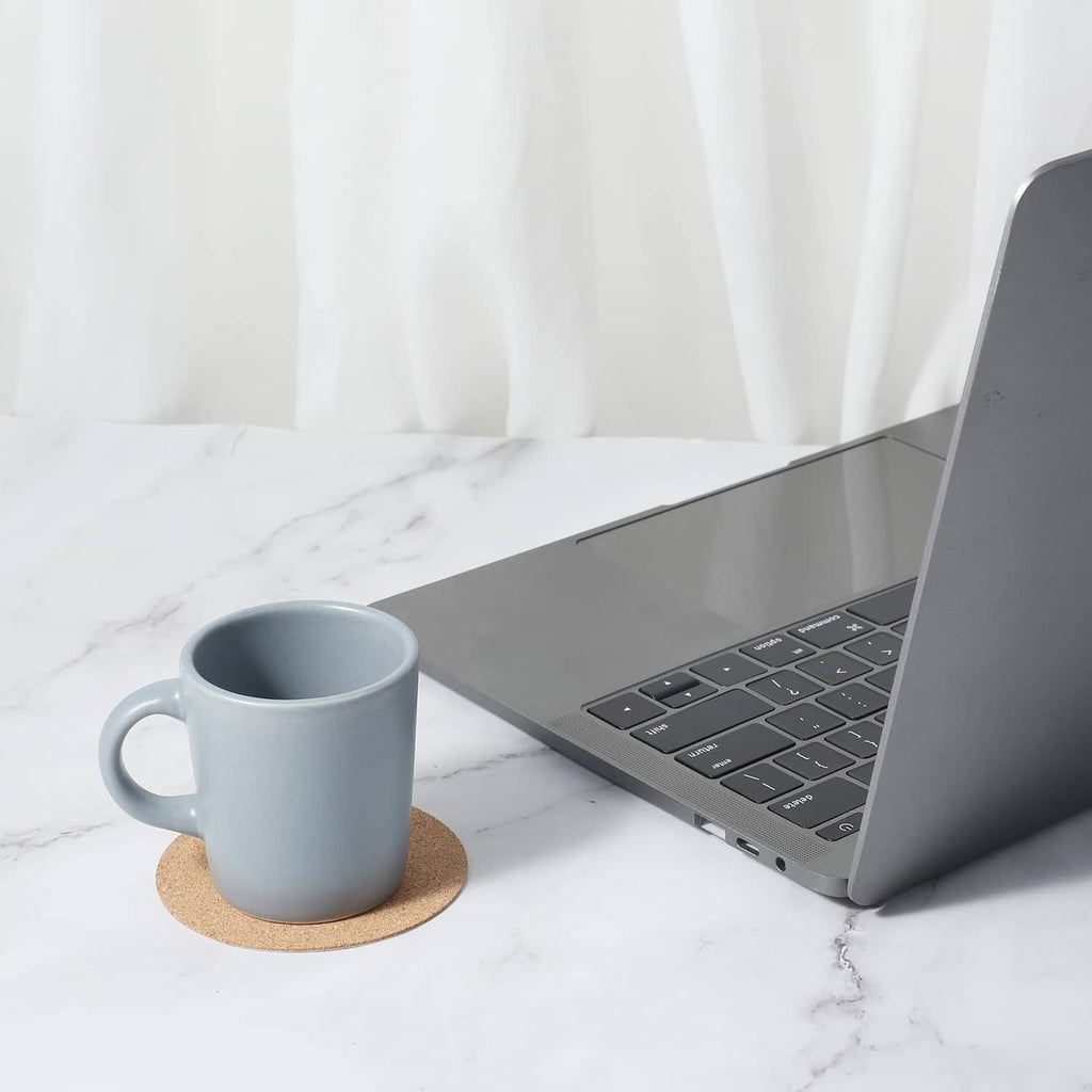 Cork round coaster under a blue mug next to a laptop