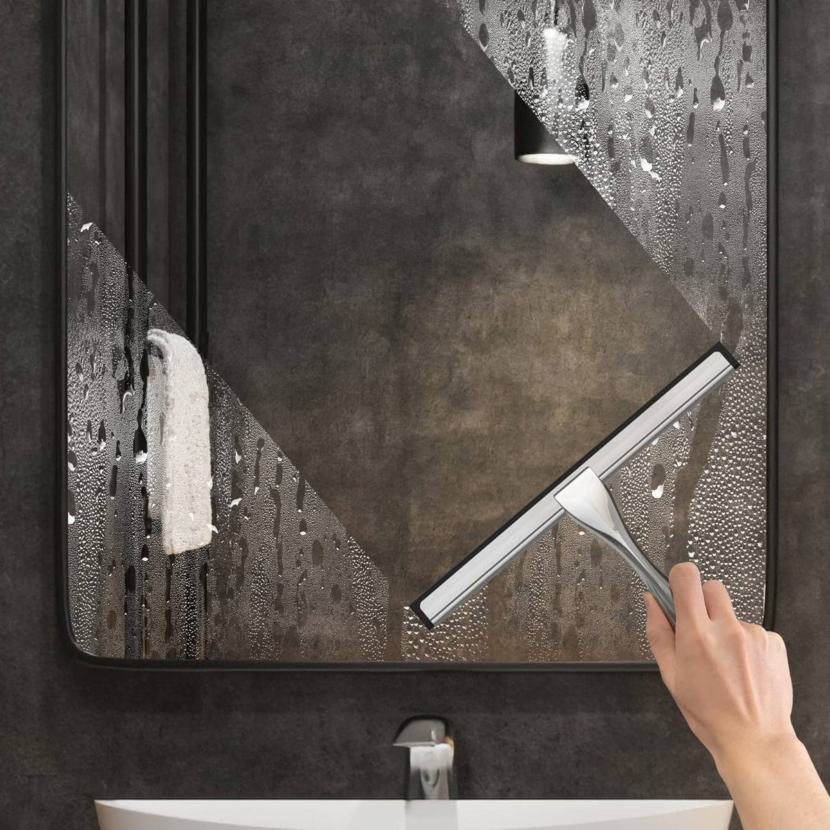 Handheld stainless steel squeegee clearing water from shower glass.