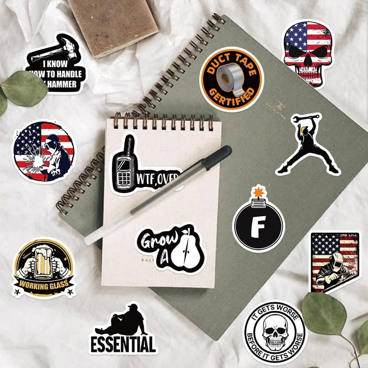 Assorted hard hat stickers with icons and sayings, scattered on notebooks and cards