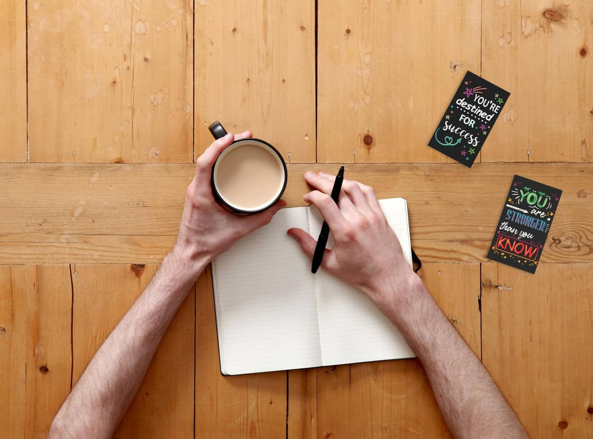 Set of mini motivational cards on a wooden table, one card held near marker