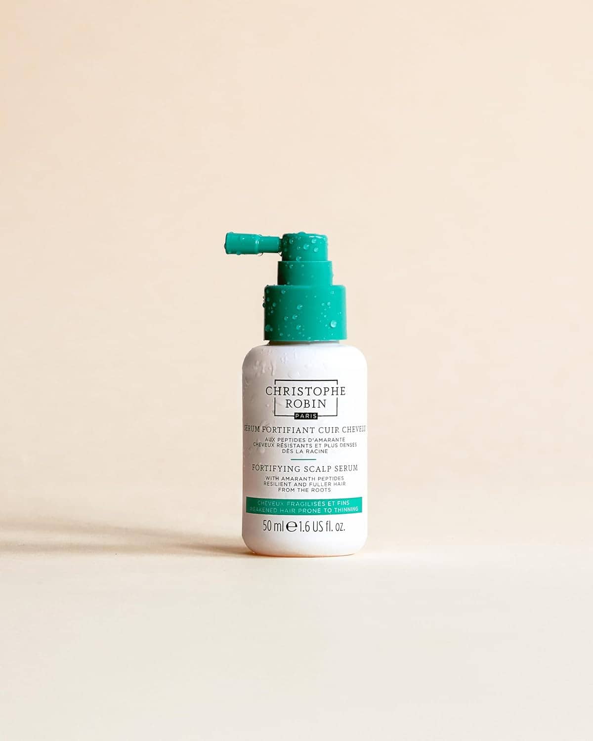Fortifying scalp serum bottle with teal pump centered on a light surface