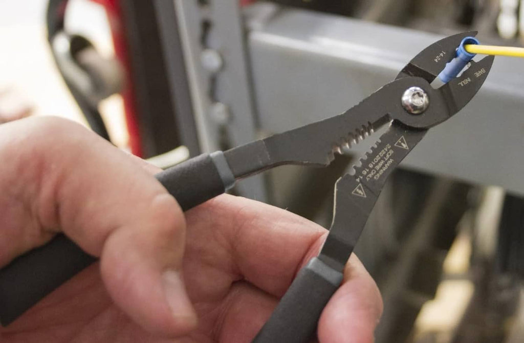 Hand holding black multi-function wire stripper pliers near a blue wire