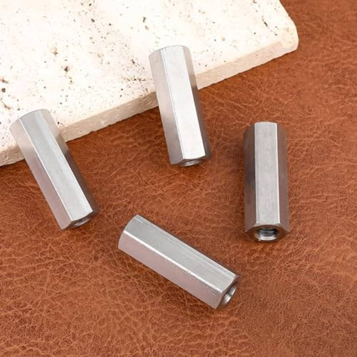 Hex coupling nuts scattered on surface, silver metal, visible threaded openings