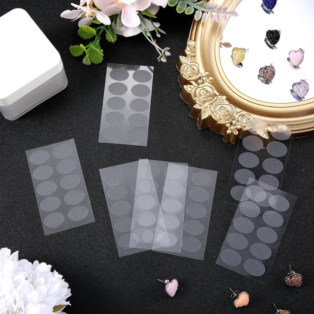 Clear oval earring adhesive sticker pads scattered on a dark surface